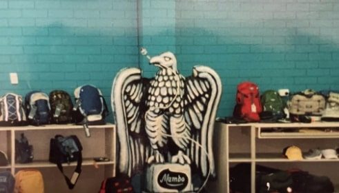 An statue of an eagle in a room filled with bags, shoes, and cup in a skyblue wall.